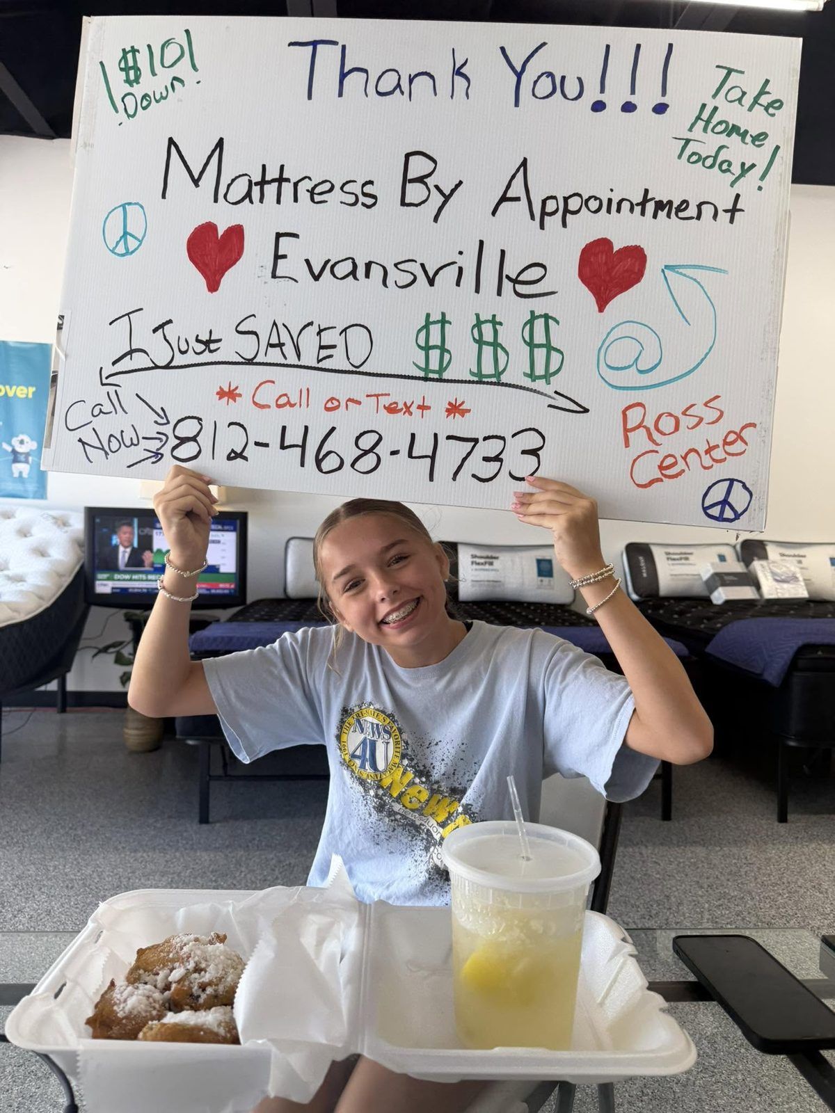 Young customer holding a handwritten Mattress By Appointment thank-you sign overhead