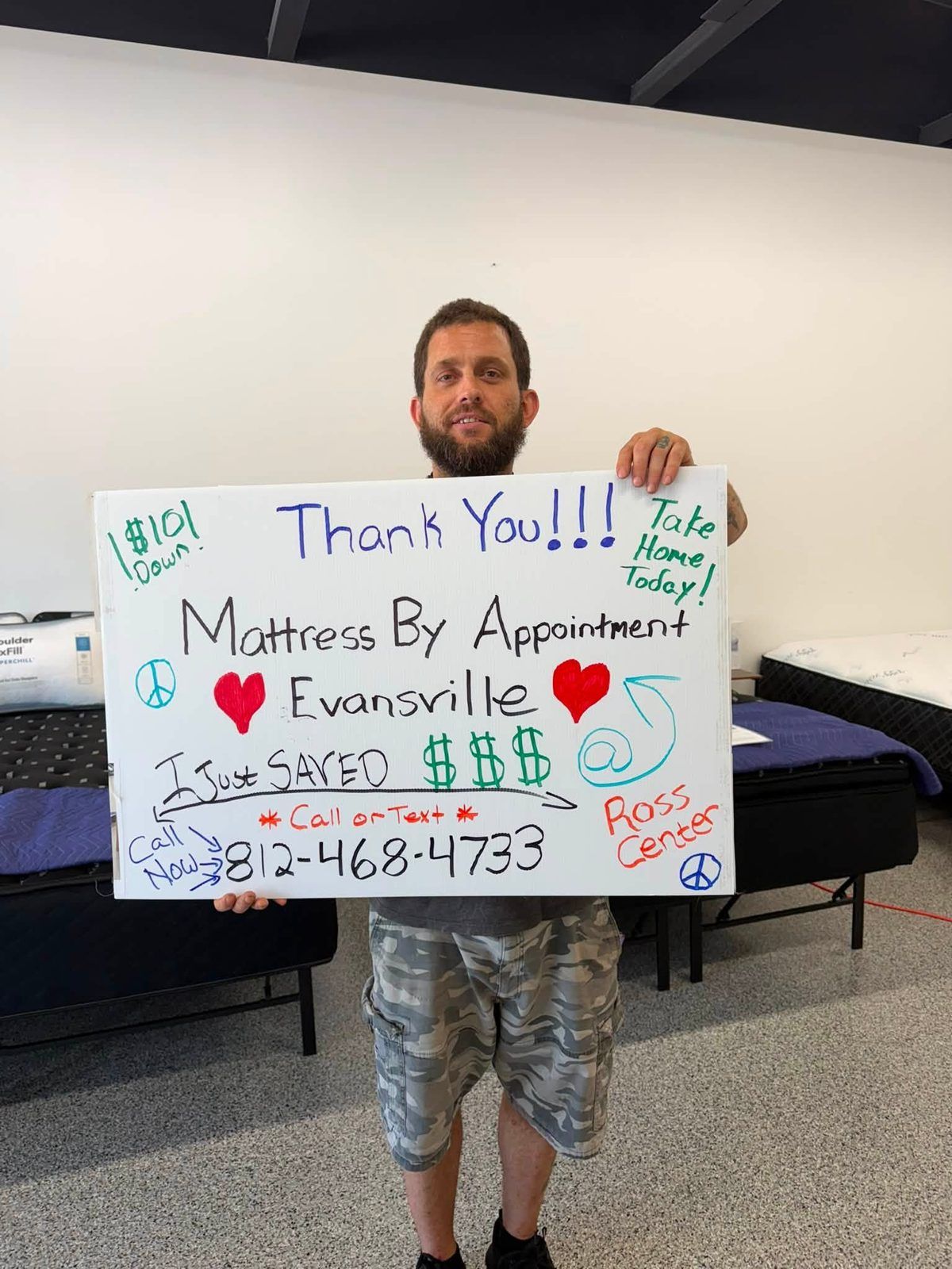Customer in the showroom holding a handwritten Mattress By Appointment thank-you sign