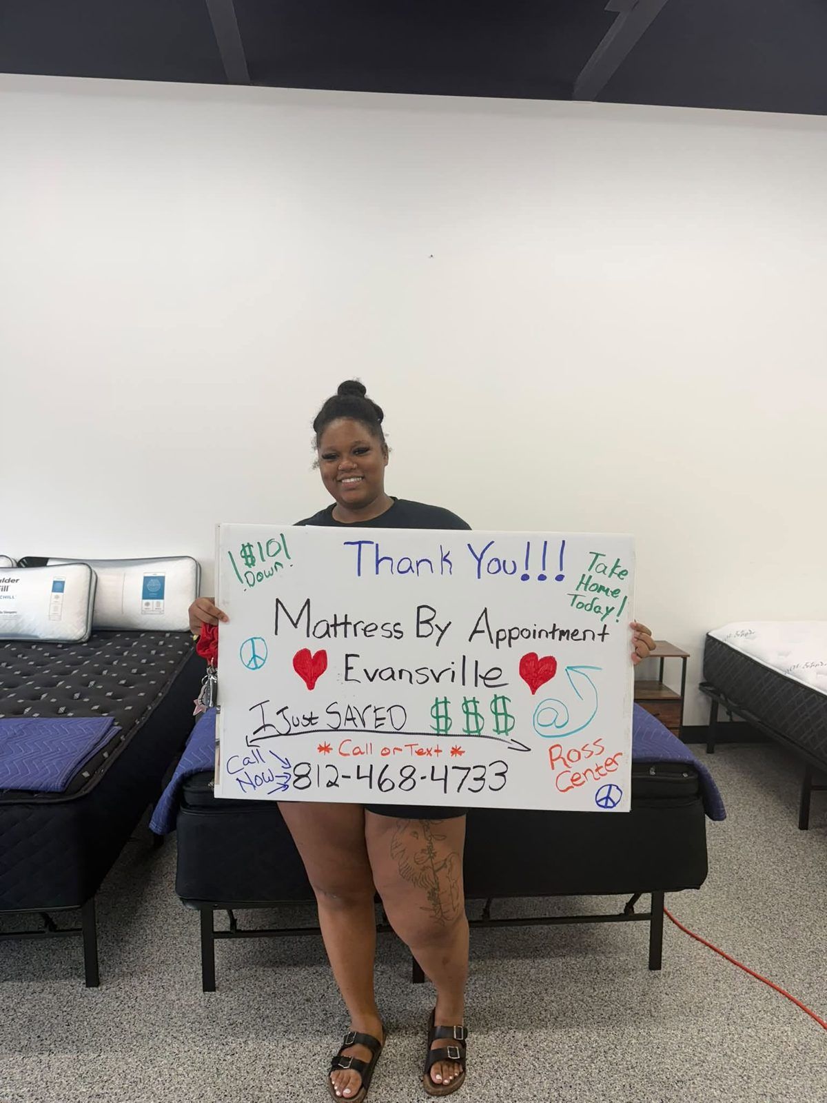 Customer in the showroom holding a handwritten Mattress By Appointment thank-you sign