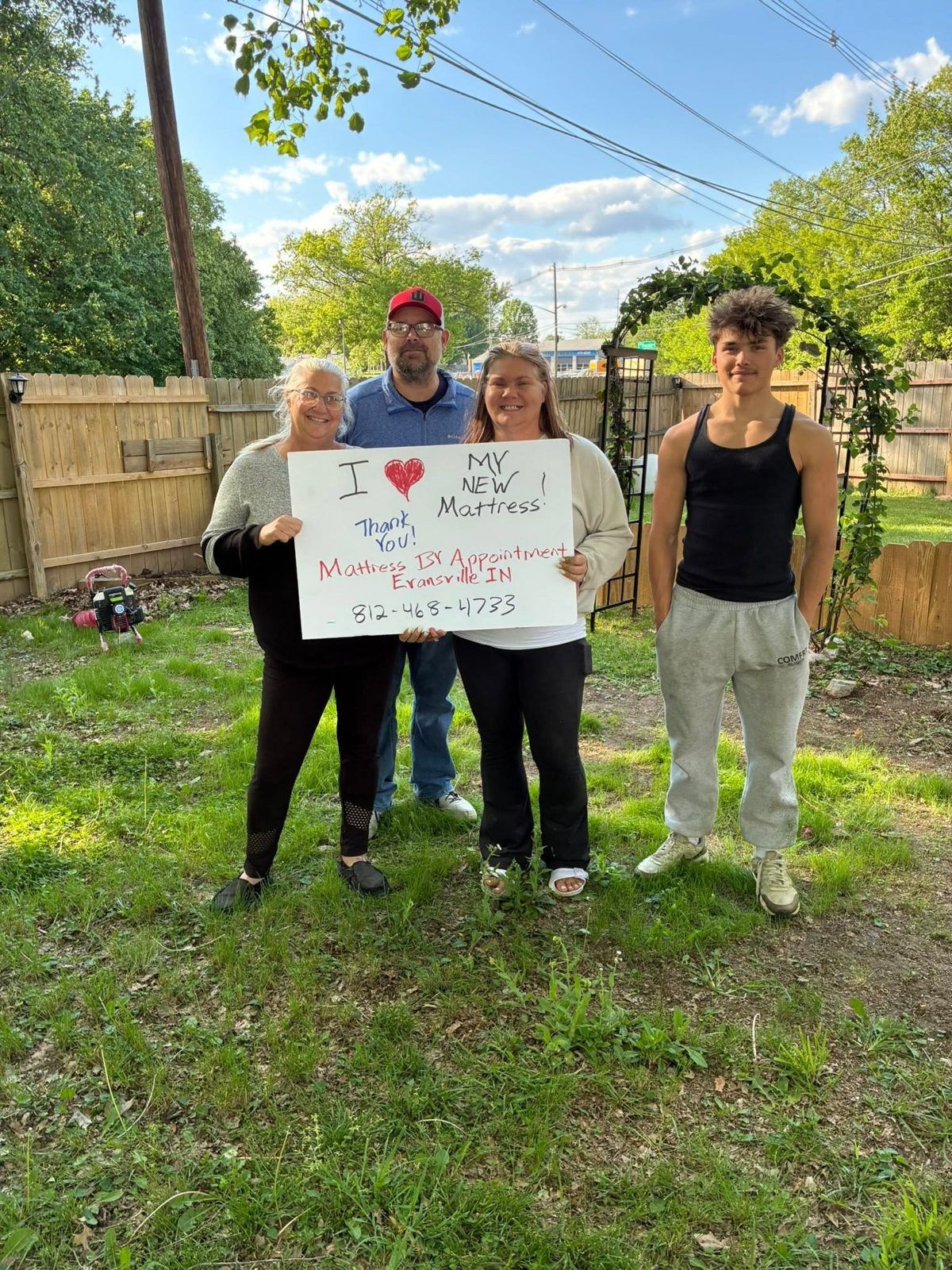 Four customers outdoors holding an “I love my new mattress” sign