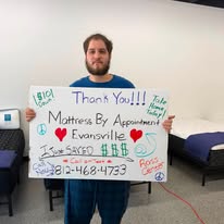 Customer in a blue shirt holding a handwritten thank-you sign in the showroom