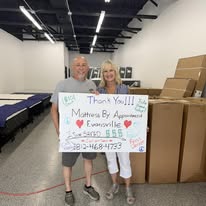 Two customers holding a handwritten thank-you sign among boxes in the showroom