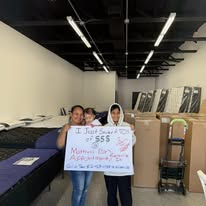 Customers holding a handwritten thank-you sign among boxes in the showroom