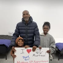 Man and two children holding a handwritten sign about their new mattress