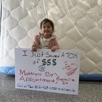 Child sitting on a mattress behind a handwritten sign