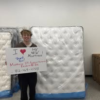 Person standing between mattresses holding a handwritten sign